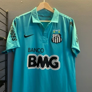 Turkos fotbollströja från Nike - Säljer en turkos fotbollströja från Nike med Santos FC-logga och sponsortryck. Tröjan har korta ärmar och nummer 11 med Neymar Jr på ryggen. Perfekt för fotbollsfans! Replika i storlek L helt ny med tagg