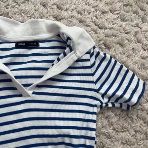 Randig pikétröja från Sinsay - Säljer en snygg randig pikétröja från Sinsay i storlek XS. Tröjan har blå och vita ränder med en klassisk krage och korta ärmar. Perfekt för en avslappnad stil. 🌀Inga defekter, knappt använd🩷
