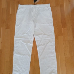 Nya  linnebyxo, strl XLr från Jack & Jones - Säljer ett par vita avslappnade byxor från Jack & Jones i storlek XL. Byxorna har en elastisk midja med snörning och är tillverkade i ett lätt och bekvämt material. Perfekta för en avslappnad stil.