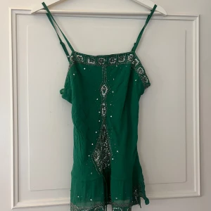 Grön ärmlös topp med paljetter - Snygg grön ärmlös topp med tunna axelband och dekorativa paljetter. Perfekt för en festlig kväll med sin glittrande design. Säljer då den är för liten