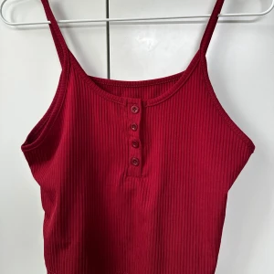 Röd ribbad linnetopp - Säljer en snygg röd ribbad linnetopp med knappar framtill. Perfekt för varma dagar eller som ett lager under en jacka. Den har smala axelband och en bekväm passform.