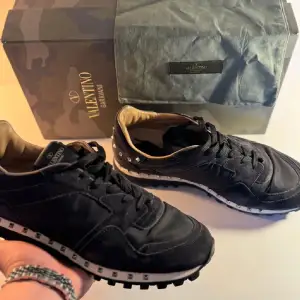 Snygga svarta sneakers från Valentino Garavani med ikoniska nitar runt hälen och sulan. Skorna har en stilren design med snörning och en bekväm passform. Perfekta för att ge din outfit en lyxig touch.