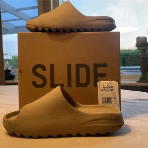 Beige Adidas Yeezy Slide - Säljer ett par bekväma och stilrena beige Adidas Yeezy Slide. Perfekta för en avslappnad look med sin minimalistiska design och mjuka material. De har en vågig sula för extra grepp och komfort.