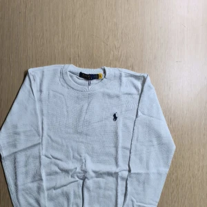 Vit tröja från Ralph Lauren - Säljer en stilren vit tröja från Ralph Lauren. Tröjan har en klassisk rund hals och långa ärmar. Perfekt för en elegant och avslappnad look. Märkets ikoniska logga är broderad på bröstet.