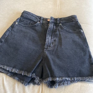 Svarta jeansshorts - Snygga svarta jeansshorts från h&m med fransiga kanter. Perfekta för en avslappnad stil. De har klassiska femficksdetaljer och en knappgylf.