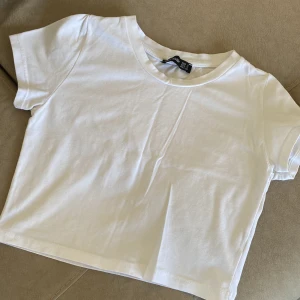 Vit croppad t-shirt från H&M - Säljer en stilren vit croppad t-shirt från H&M. Perfekt för en avslappnad look. T-shirten har korta ärmar och är gjord i mjuk bomull. Passar perfekt till jeans eller kjol!