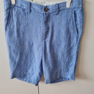 Blå linneshorts från Crewcuts (barn) - Snygga blå linneshorts från Crewcuts i storlek 12. De är tillverkade i ett lätt och bekvämt material, perfekt för varma dagar. Shortsen har en knapp och dragkedja framtill samt fickor både fram och bak. Midja 72cm. Längd 43cm. Kan hämtas i Vallentuna.