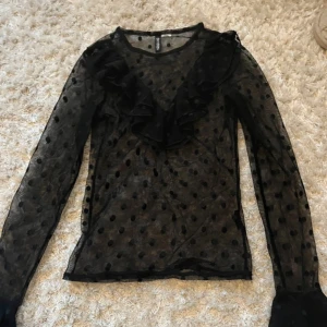 Svart blus från H&M  - Snygg svart transparent blus från H&M Divided med prickigt mönster och volangdetaljer framtill. Står ingen storlek men skulle säga att de är en XS 