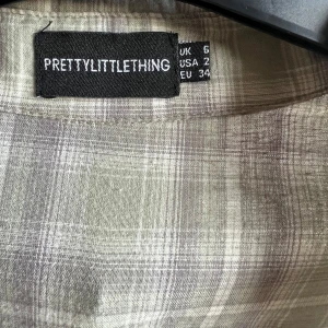 Rutig skjorta från PrettyLittleThing - Säljer en stilren rutig skjorta från PrettyLittleThing i ljusa toner. Skjortan har långa ärmar och knappar framtill samt två bröstfickor med knappar. Perfekt för en avslappnad look.