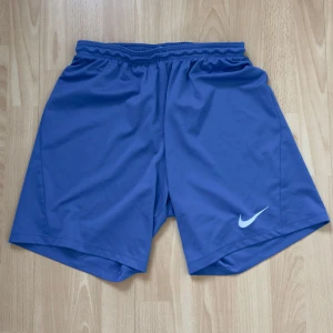 Blå träningsshorts från Nike - Snygga blå träningsshorts från Nike med elastisk midja och det klassiska Nike-loggan i vitt. Perfekta för sport och träning med en bekväm passform.