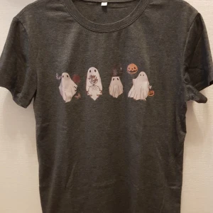 Grå t-shirt med trek or treat spökmotiv - Säljer en grå t-shirt med ett coolt spökmotiv på framsidan. Perfekt för Halloween eller bara för att rocka en unik stil. T-shirten har korta ärmar och är gjord i mjukt material för extra komfort. 🎃👻