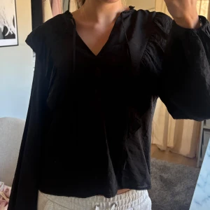 Svart blus med knytband -  svart blus med v-ringning och knytband vid halsen. Tunt material så den passar för sommaren och våren. Man kan knyta den eller ha den öppen