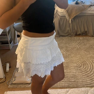 Vit kortkjol med spetsdetaljer - Säljer en söt vit lågmidjad kortkjol med  spetsdetaljer. Perfekt för varma sommardagar! Köpte på en Saco hand butik 