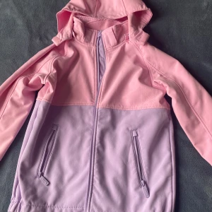 Rosa och ljuslila jacka med huva - Säljer en snygg rosa och ljuslila jacka med huva. Jackan har dragkedja framtill och två praktiska fickor med dragkedjor. Perfekt för vår och sommar!