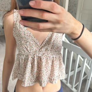 Blommig ärmlös topp - Söt blommig topp med volangdetaljer och v-ringning. Toppen är ärmlös och har en luftig passform med elastisk rygg för extra komfort. Perfekt för varma dagar!