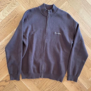 Brun kofta från Sweet Sktbs - Säljer en zip sweater från Sweet Sktbs med ribbad krage. Koftan har ett broderat märke på bröstet och text på ryggen. Oanvänd.