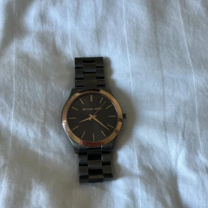 Svartgrå klocka från Michael Kors - Snygg svartgrå klocka från Michael Kors med stilren design. Klockan har en svart urtavla och metallarmband. Perfekt accessoar för att komplettera din look. Fick den här om dagen som present men har ingen användning av den. Nypris är på 2300 jag säljer den för 1500
