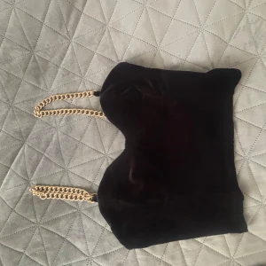 Svart fest topp med guldkedja - Elegant svart fest topp  i mjukt material med en stilren guldkedja som axelrem. Perfekt för att ge en touch av lyx till din outfit.
