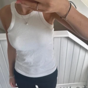 Vit ärmlös linnetopp - Säljer en stilren vit ärmlös linnetopp. Perfekt för varma dagar eller som ett basplagg i garderoben. Toppen har en rund halsringning och är gjord i ett mjukt material.