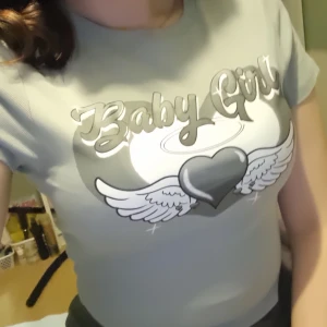 Grå t-shirt med tryck från FB Sister - Säljer en grå t-shirt från FB Sister med ett coolt tryck av texten 'Baby Girl' och ett hjärta med vingar. Perfekt för en avslappnad stil. 💫