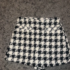 Svartvita rutiga shorts - Snygga svartvita shorts med ett klassiskt rutigt mönster. De är en kjol där fram och shorts där bak. Så man kan säga att det är en mix av båda. De är högmidjade och har en stilren design som passar perfekt för en trendig look. Materialet känns bekvämt och ger en chic touch till din outfit. Aldrig använd. Prislapp är kvar på.