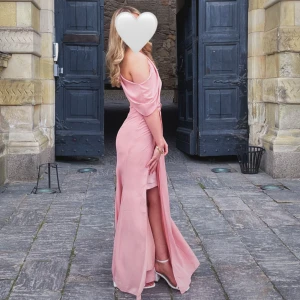 Rosa axelbandslös långklänning - Elegant rosa långklänning med offshoulder-design och en smickrande slits. Perfekt för festliga tillfällen. Klänningen har en vacker drapering och en figurnära passform. Perfekt nu ifall man ska ha bal eller skolavslutning! Endast en gång användning! Priset går att diskutera