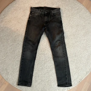 Svarta lean Dean från Nudie Jeans - Snygga svarta jeans från Nudie Jeans med en tight passform. De har en klassisk femficksdesign och en knappgylf. Perfekta för en stilren look.