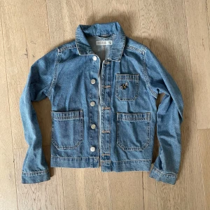 Jeansjacka från Cubus  - Säljer en klassisk jeansjacka från Cubus med knappar framtill och tre praktiska fickor. Jackan har en stilren design med långa ärmar och är perfekt för vår och sommar. Perfekt för att ge din outfit en cool touch!