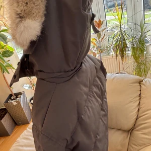 Grå dunjacka från Canada Goose - Säljer en stilren grå dunjacka från Canada Goose med pälskantad huva. Jackan har knappar och en quiltad design som ger extra värme. Perfekt för kalla dagar.
