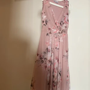 Rosa blommig klänning från Bodyflirt - Säljer en romantisk rosa klänning från Bodyflirt med vackert blommönster. Klänningen har en omlott-design och är ärmlös med en v-ringad hals. Perfekt för sommarens festligheter! 🌸