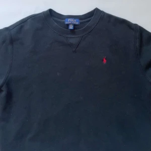 Svart tröja från Polo Ralph Lauren - Säljer en klassisk svart tröja från Polo Ralph Lauren med det ikoniska röda logotypbroderiet på bröstet. Tröjan har rund hals och långa ärmar, perfekt för en stilren look. Pris kan diskuteras 