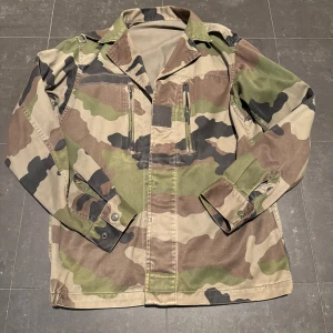 Camouflage militärjacka - Säljer en cool militärjacka i klassiskt camouflagemönster. Jackan har långa ärmar och praktiska dragkedjor framtill. Perfekt för dig som gillar en tuff stil. Passar S men upp till M.