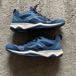 Blå sneakers från Mizuno - Snygga blå sneakers från Mizuno med vita detaljer och svart-vita snören. Skorna har en sportig design med meshpaneler för extra ventilation och en robust, mönstrad sula. Perfekta för dig som gillar en aktiv livsstil och vill ha stilrena träningsskor.