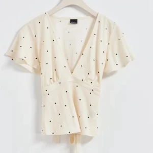 Beige prickig topp från Gina tricot - Säljer nu min sååå snygga beige blus från Gina Tricot med svarta prickar och v-ringning. Blusen har korta ärmar och en knytning i midjan som ger en fin passform. 