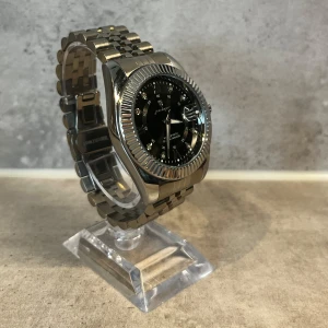 Svart Poedagar Premium klocka 40mm - Stilren klocka från Poedagar i silverfärgat rostfritt stål med länkarmband och svart urtavla. Urtavlan har markerade index med små stenar och datumvisning. Klassisk rund boett och räfflad kant ger en lyxig känsla. Perfekt accessoar för dig som gillar snygga detaljer. Box, extra länkar, länkjusterare & silkesduk medföljer. PRISET KAN DISKUTERAS VID SNABB AFFÄR.
