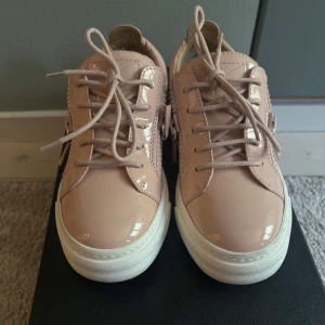 Gammelrosa sneakers från Giuseppe Zanotti - Snygga sneakers i blankt gammelrosa skinn från Giuseppe Zanotti. Skorna har vita platta sulor, snörning och dragkedjor på sidorna för extra edge. Perfekt för dig som gillar stilrena men ändå unika detaljer. Endast använda en gång! Boxen följer med :)