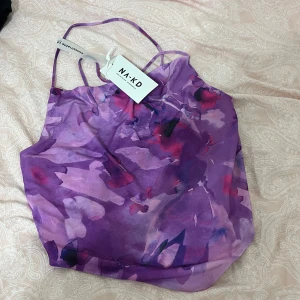 Lila blommig linnetopp från NA-KD - Supersöt linnetopp från NA-KD med blommigt mönster i olika lila och rosa nyanser. Tunt och lätt material med smala axelband och croppad passform. Perfekt för sommarens alla tillfällen när du vill sticka ut lite extra.