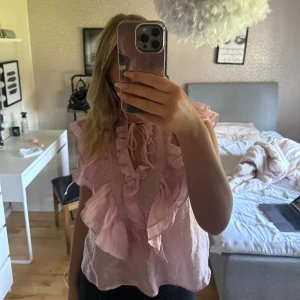 Ljusrosa blus med volang och knyt - Supersöt ljusrosa blus med volanger längs v-ringningen och knytband vid halsen. Luftig och lätt i materialet, perfekt för vår och sommar. Blusen är köpt från Kappahl. Har aldrig använt den utan bara testad och lappen är kvar.. Den är i storlek XS, men säljer även en i S också. Nypris 399kr🤍