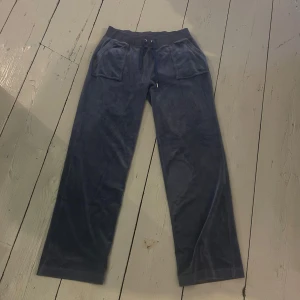Mörkblå velourbyxor Juicy Couture - Mysiga mörkblå mjukisbyxor från Juicy Couture i mjuk velour. Byxorna har raka ben, bred resår i midjan med snörning och stora fickor både fram och bak. Broderad JC-logga framtill. Perfekta för chill eller streetstyle. Dom har ett litet hål på en sida längst ner vid benet men syns knappt, på ena snöret saknas även den ena metall biten men dom är fortfarande i väldigt bra skick skriv för mer info!. 