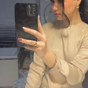 Beige långärmad klänning med öppen rygg - Säljer en beige långärmad klänning i satinliknande material. Klänningen har öppen rygg med knytband i nacken och är ”delade” länges ut vid ärmarna! Har andvänt den enbart en gång och priset går att diskutera vid snabb köp🫶🏼