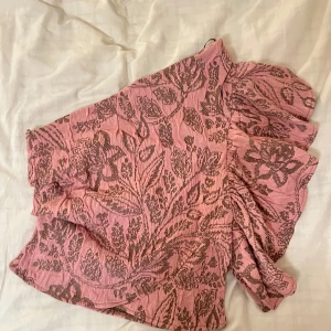  Boho oneshoulder topp  - Superfin rosa topp med blommigt mönster och volangdetalj på ena axeln. One shoulder-modell.