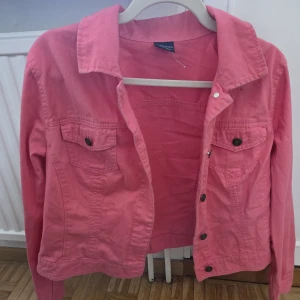 Rosa jeansjacka från Faded Glory - Snygg rosa jeansjacka från Faded Glory i 100% bomull. Klassisk modell med krage, bröstfickor med knappar och knappstängning framtill. Perfekt för dig som vill sticka ut med färg och ha en jacka som funkar till många olika outfits.