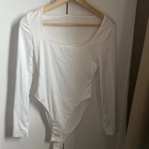 Långärmad body med fyrkantig ringning - Tre långärmade bodies i vitt, grått och svart med snygg fyrkantig ringning. Tight passform och mjukt stretchigt material som sitter perfekt. Perfekt att styla med jeans eller kjol för en clean look. Knäppning i grenen för enkel användning.