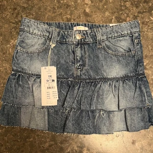 Jeanskjol med volang från Gina Tricot - Snygg blå jeanskjol från Gina Tricot med låg midja och volangdetaljer. Kjolen har klassiska fickor, bälteshällor och råa kanter för en trendig look. Perfekt för dig som gillar denim och vill ha en cool stil. Helt ny, oanvänd, med lapparna kvar! Helt slutsåld på Gina Tricot💓💓