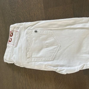 Vita skinny jeans från Dondup (små i storlek) - Snygga vita jeans från Dondup med skinny fit och klassisk femficksdesign. Byxorna har knäppning med knappar framtill och diskret Dondup -logga på bakfickan. Perfekta för dig som vill ha en fräsch och stilren look. Byxorna är hela men något slitna i färgen på vissa ställen.
