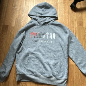 Grå tracksuit från Trapstar - Säljer ett par grå tracksuit från Trapstar med tryckt logga i rött, svart och vitt på ena benet. Byxorna har resår i midjan och vid bensluten för en skön och avslappnad passform. Perfekta för chill eller streetwear vibes.