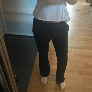 Svarta utsvängda kostymbyxor - Säljer ett par svarta kostymbyxor med utsvängd passform och låg midja. Byxorna har klassisk look och är perfekta om du vill ha en clean och stilren vibe. Materialet känns mjukt och följsamt, och de sitter snyggt över höfterna.