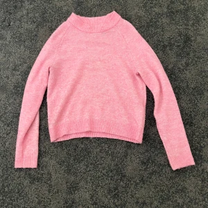 Rosa stickad tröja med ribbade detaljer - Mysig rosa stickad tröja med ribbade muddar vid ärmslut, nederkant och halsringning. Lite nopprig men går att ta bort, därav priset.