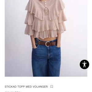 Beige stickad topp med volanger - Superfin beige stickad topp med flera lager volanger och knytning med små knappar vid halsen. Croppad modell som ger en cool och trendig look. Perfekt att styla med jeans eller kjol för en extra touch. Aldrig använd, från Zara 250 kr. 