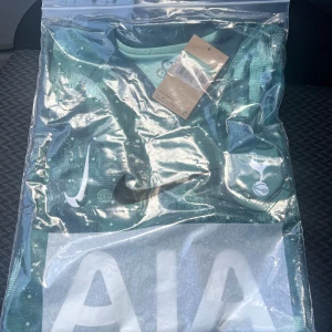 Tottenham Hotspur Nike fotbollströja - Snygg Tottenham Hotspur fotbollströja från Nike i en mörkgrön nyans med ljusgröna detaljer och prickigt mönster. Tröjan har korta ärmar, klubbmärke på bröstet och stor vit AIA-logga framtill. Perfekt för dig som vill sticka ut på planen.